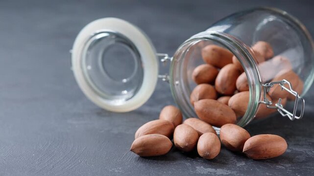 pecan were poured out of a glass storage jar onto on a black stone table.