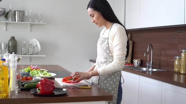 young asian woman in apron cutting bell pepper for salad at home in kitchen, korean girl cooking healthy food at home and cutting vegetables