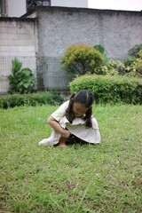 Young Girl Exploring the Grass in the Back Garden of the House, in a squatting position while...