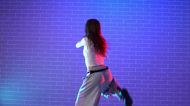 young crazy girl dancing hip hop against wall background in neon lighting, female choreographer moving to music and performing jazz funk in dance studio