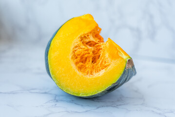 Sliced pumpkin revealing vibrant orange flesh, displaying textured rind on pristine marble surface