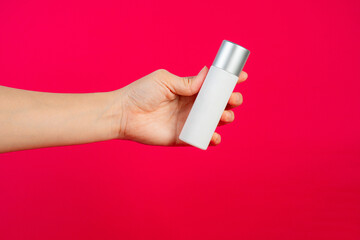 Skin care or sunscreen cosmetic and hand on red background.