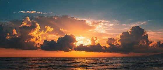 Dramatic sunset over a calm ocean.  A fiery orange and gold sunset illuminates a sky filled with dramatic clouds, casting a warm glow over the tranquil ocean surface
