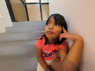 A young girl sitting on stairs with a dreamy expression, looking upward with imagination. A simple,...