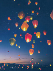 Fototapeta premium A breathtaking scene of countless glowing lanterns floating into a deep blue night sky during a lively lantern festival. 