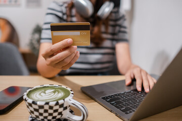 A woman uses a laptop and credit card for online shopping in a cafe, with a matcha latte and...