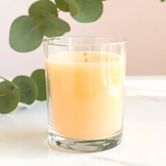 Fototapeta premium Glass Candle with Yellow Wax and Eucalyptus Leaves.