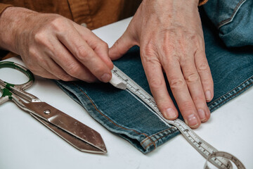 hands skillfully use chalk to mark denim fabric for alterations, demonstrating art tailoring in small business environment. tools like scissors and ruler enhance craft. close up.