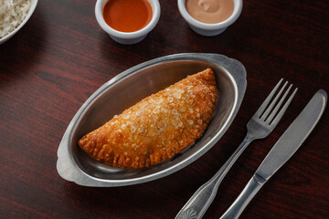 Close-up overhead view of a freshly fried empanada with golden crunchy texture, served with dipping...