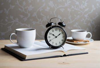Alarm clock next to notebook and coffee cup on table