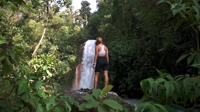 Woman standing on a large rock with las Gemelas Waterfalls cascading behind them.