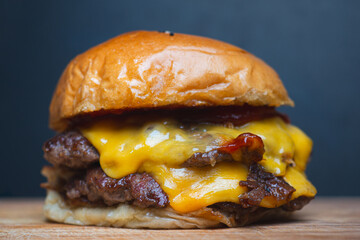 Double beef cheeseburger with melted cheddar and glossy bun on wooden board close-up.