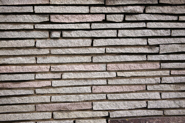 Close-up of a stacked stone wall with narrow rectangular slabs arranged in a horizontal pattern.