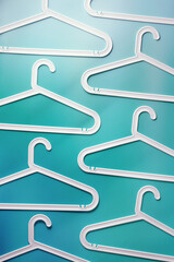 Top view minimal style pattern of white plastic hangers with hooks on teal blue background. Flat...