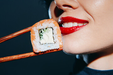 Bright and vivid close-up of a woman's smile with red lipstick, holding sushi with chopsticks,...