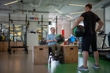 Wheelchair athlete trains with medical ball with personal couch in gym. Spinal injury...