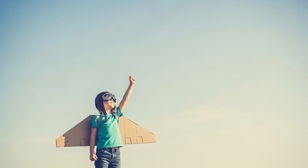Child with cardboard wings pretends to fly against a clear blue sky