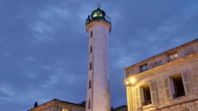 Quai Valin lighthouse beside historic building under twilight sky, La Rochelle, Charente-Maritime, France.