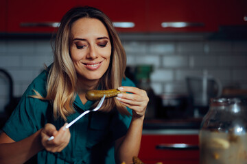 Happy Smiling Woman Holding a Pickle in a Fork. Cheerful housewife testing freshly marinated cucumbers 
