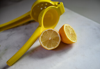 A yellow lemon juicer showcasing a halved lemon on a marble counter.