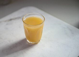 A glass of refreshing orange juice on a light marble background.