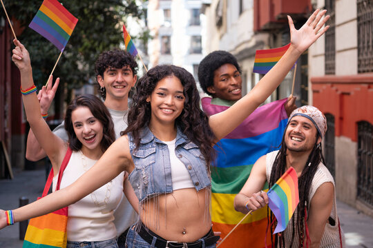 Portrait of diverse group of young people waving rainbow flags, celebrating lgbtq pride and equality during a vibrant street parade - Powered by Adobe