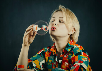 Blonde woman blowing big soap bubble on dark background