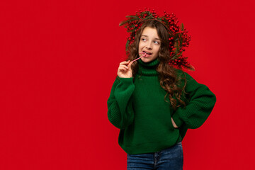 Young girl in a green sweater biting a candy cane while looking sideways, appearing thoughtful