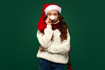 Girl in Santa hat holding pompom to her nose in a fun pose
