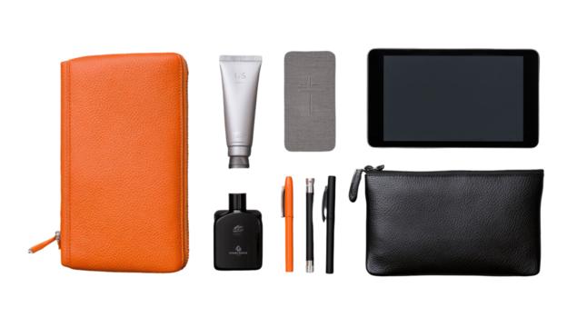 Flat lay of travel accessories.  Orange leather zip case, light beige/cream tube, grey rectangular object, black tablet, black pouch, small dark bottle, pen, orange pen cap