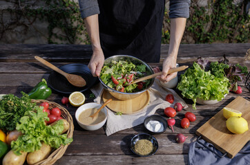A woman cooking a variety of fresh salad vegetables, tomatoes, bell pepper, potato, fruits and...