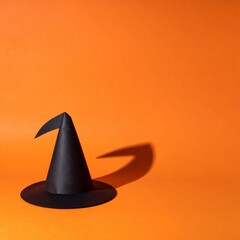 Fototapeta premium Minimalist Black Paper Witch Hat on Vibrant Orange Background in Studio Shot