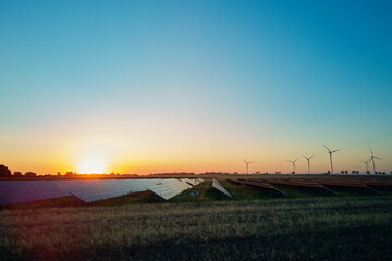 Solar panels and wind turbines in rural landscape at sunset. Concept of renewable energy,...