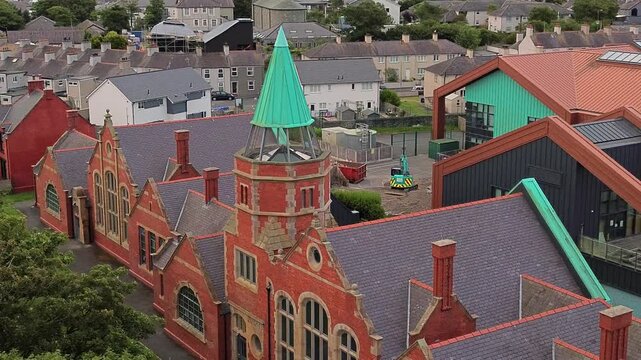 Aerial view orbiting modern vintage Welsh school with green copper spire architecture in North Wales