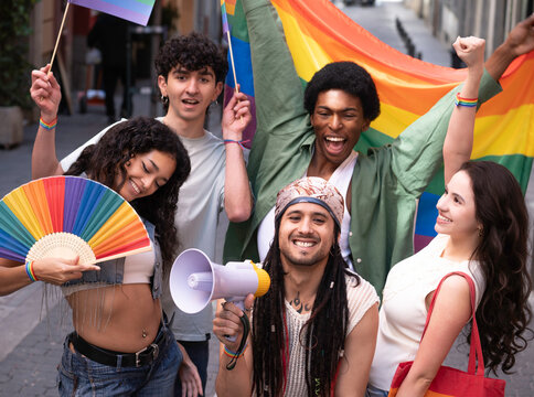 Portrait of a group of young activists holding rainbow flag and megaphone celebrating gay pride during street parade