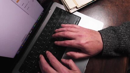 Man works from home typing on laptop keyboard in office. Top down shot