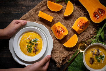 Hand holding a bowl of butternut squash cream soup