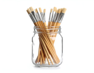 A clear glass mason jar filled with a variety of clean artist paintbrushes with wooden handles sticking out, isolated on a white background.