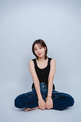 Young woman with short hair wearing a black tank top and denim jeans, sitting on the floor with a...