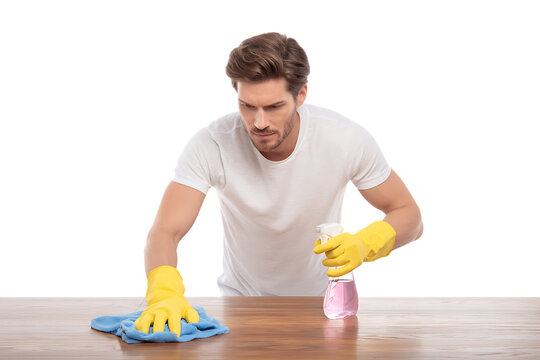Young man cleaning a wooden table with spray and cloth.