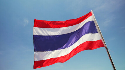The Thai national flag waving in the breeze on a tall flagpole, set against a bright and cloudless blue sky, symbolizing national pride and identity.