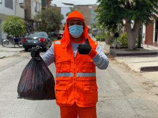 Lima, Peru - March 05, 2025: Los Olivos, Lima. A sanitation worker holds a black garbage bag while performing waste collection duties on an urban street. Ilustrative Editorial. He is wearing a bright 