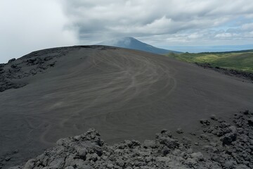 Volcanic landscape with dark ash slopes and distant misty mountain volcano