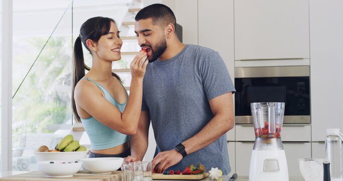 Feeding, home and couple in kitchen, strawberry and hungry with support, fruits and weight loss. Gut health, blender or man with woman, smoothie or nutrition with vitamins, relationship or eating