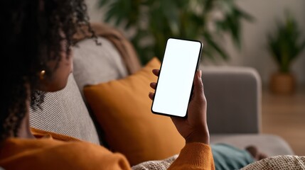 young black african woman holding smartphone in hand with white black empty mockup screen template using cell phone relaxing on sofa at home over shoulder view mobile apps advertising concept no logo