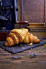 Fresh golden croissants on a rustic wooden table with lavender details and a vintage coffee grinder in the background, styled in cozy farmhouse and artisan bakery breakfast photography