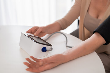 Close up of womans arm in cuff while checking blood pressure with electronic monitor in cozy modern...