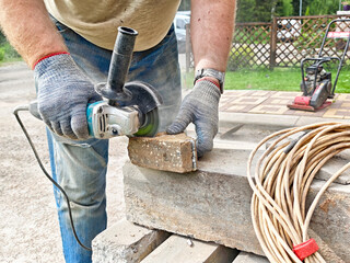 Craftsman using angle grinder to cut brick in outdoor workshop during sunny day