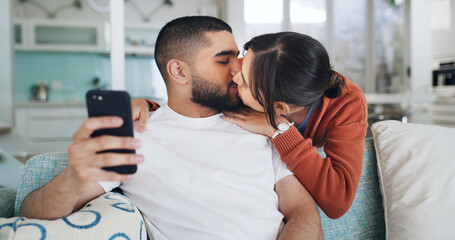 Fototapeta premium Kiss, couple and selfie in home for love, care or post on social media for relationship. Photo, man and woman in living room with picture, relax and embrace partner for romantic memory together