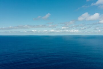 Obraz premium Expansive view of a calm, deep blue ocean under a bright sky with scattered white clouds water nature